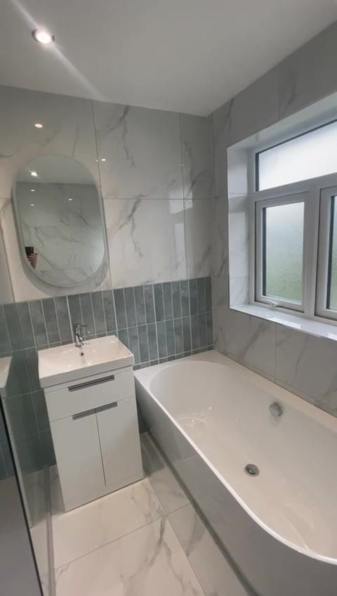 Family bathroom with marble-effect tiles, sage vertical feature tiles, white vanity unit, bath and LED mirror