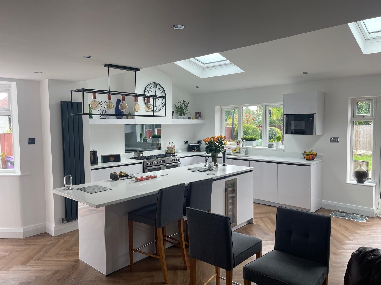 Open-plan white handleless kitchen with a large island, breakfast bar seating, roof skylights and a herringbone floor