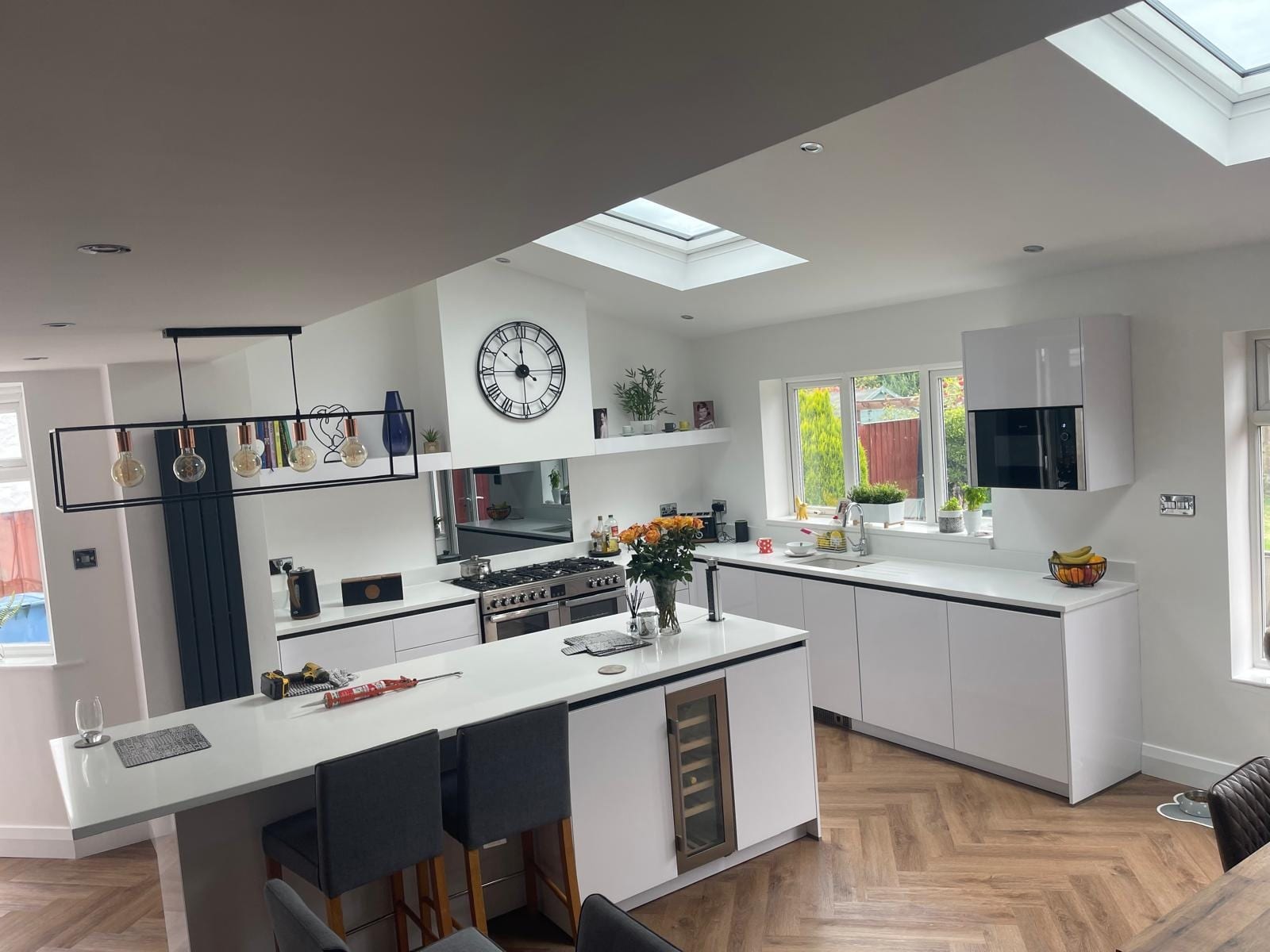 White handleless kitchen viewed across the island, with range cooker, wine cooler and herringbone wood-effect flooring
