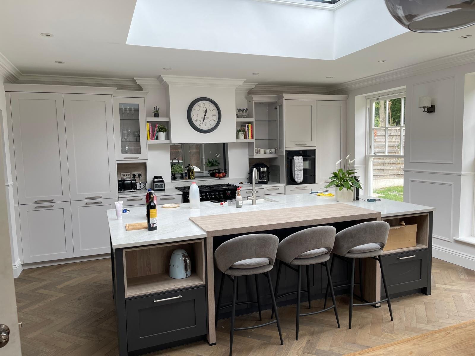 Light grey Shaker kitchen with a central island, grey velvet bar stools and a roof lantern above