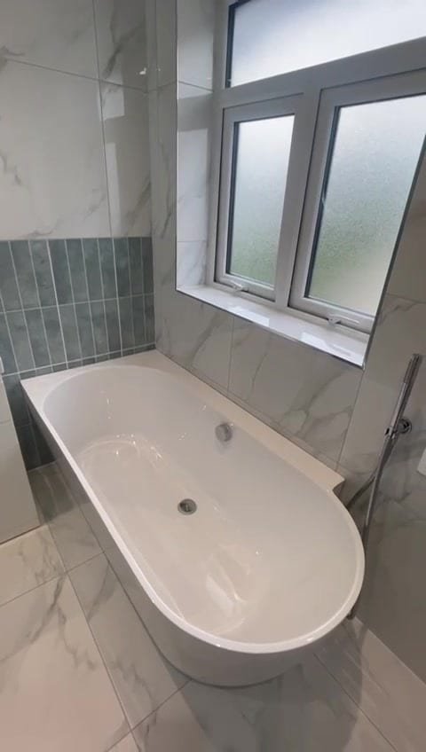 Freestanding bath against marble-effect tiled walls beneath a frosted window