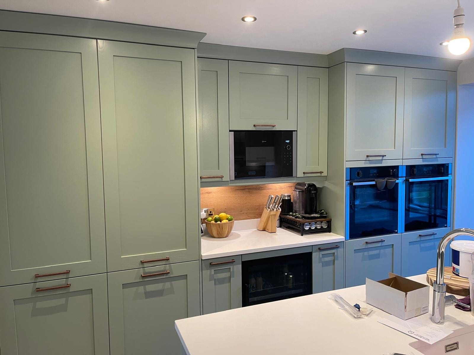 Sage green Shaker kitchen with tall larder units, built-in double oven and white quartz-effect worktops