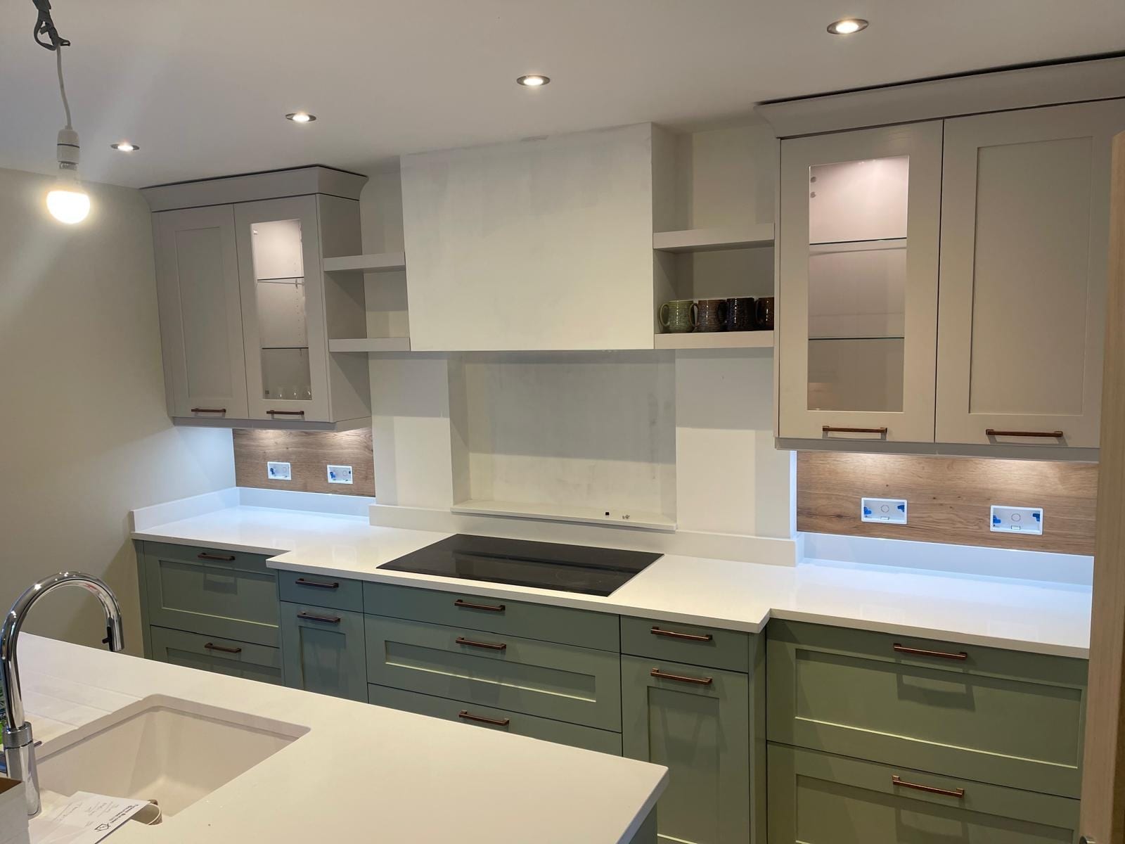 Sage green Shaker kitchen run with induction hob, extractor housing and glazed wall units